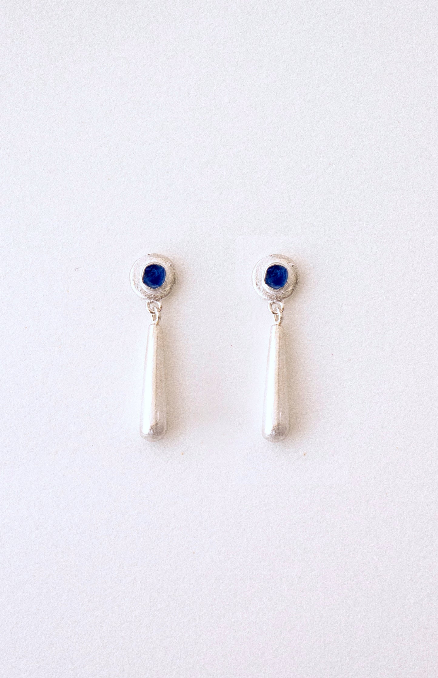 Pendienets hechos a mano con cristales azules clavados en la parte superior y caída en forma de lágrima, en plata. Artesanales con cristales del mar. Foto detalle de producto.