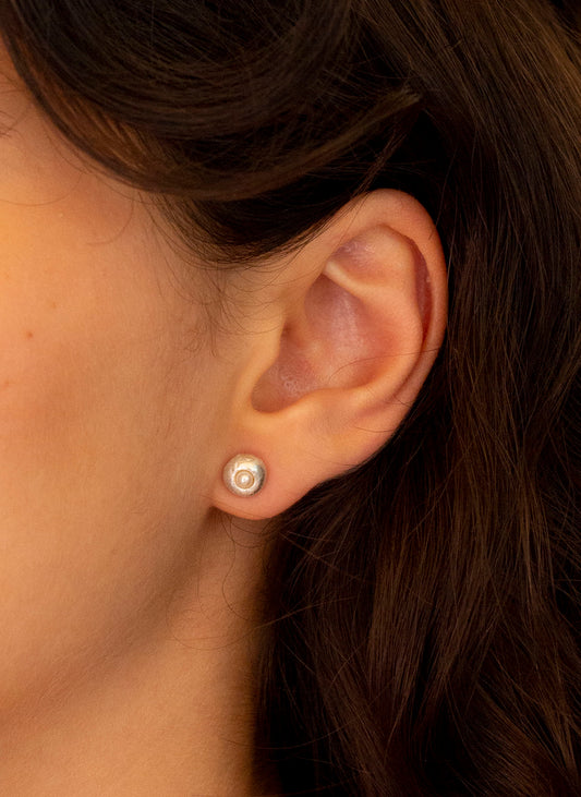 Pendientes artesanales con perla cultivada clavada en forma redonda, en plata. Foto modelo.